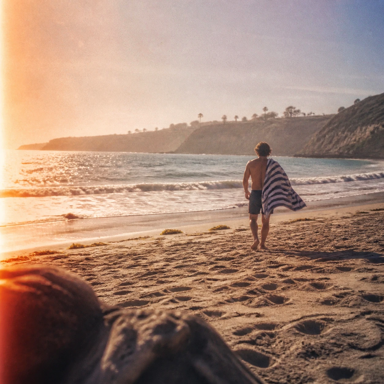 Beachgoer carrying a striped towel toward the water at sunset