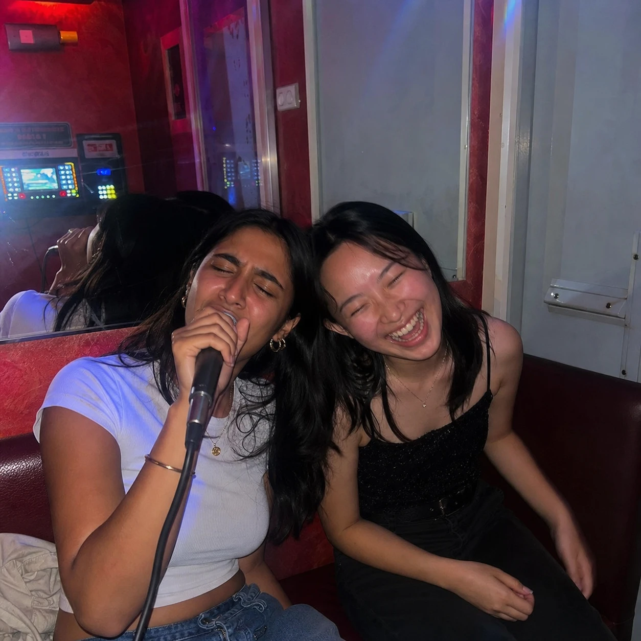 Two friends singing and laughing in a late-night karaoke room
